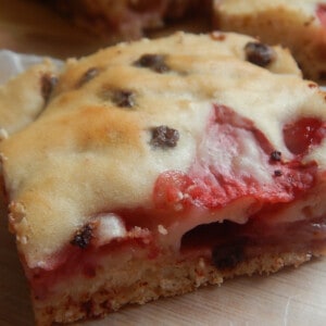 Close-up of a strawberry chocolate chip bar on parchment, cut to show the jammy strawberry layer beneath a golden top