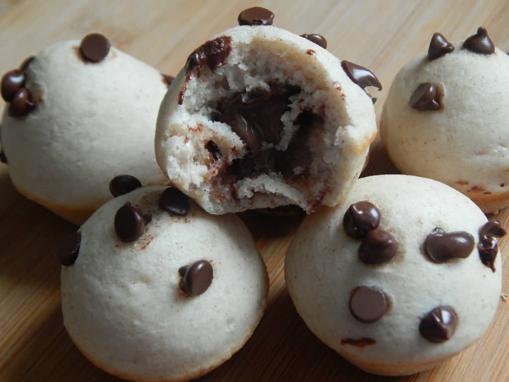 Round baked donut bites dotted with chocolate chips, one broken open to show the chocolate hazelnut filling inside