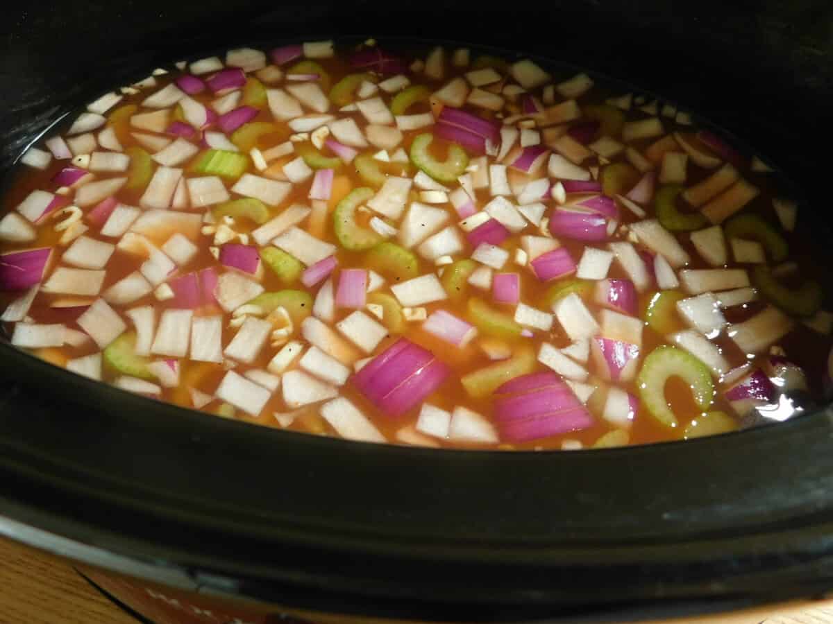 Crockpot with veggies and broth cooking with chicken for buffalo chicken. 