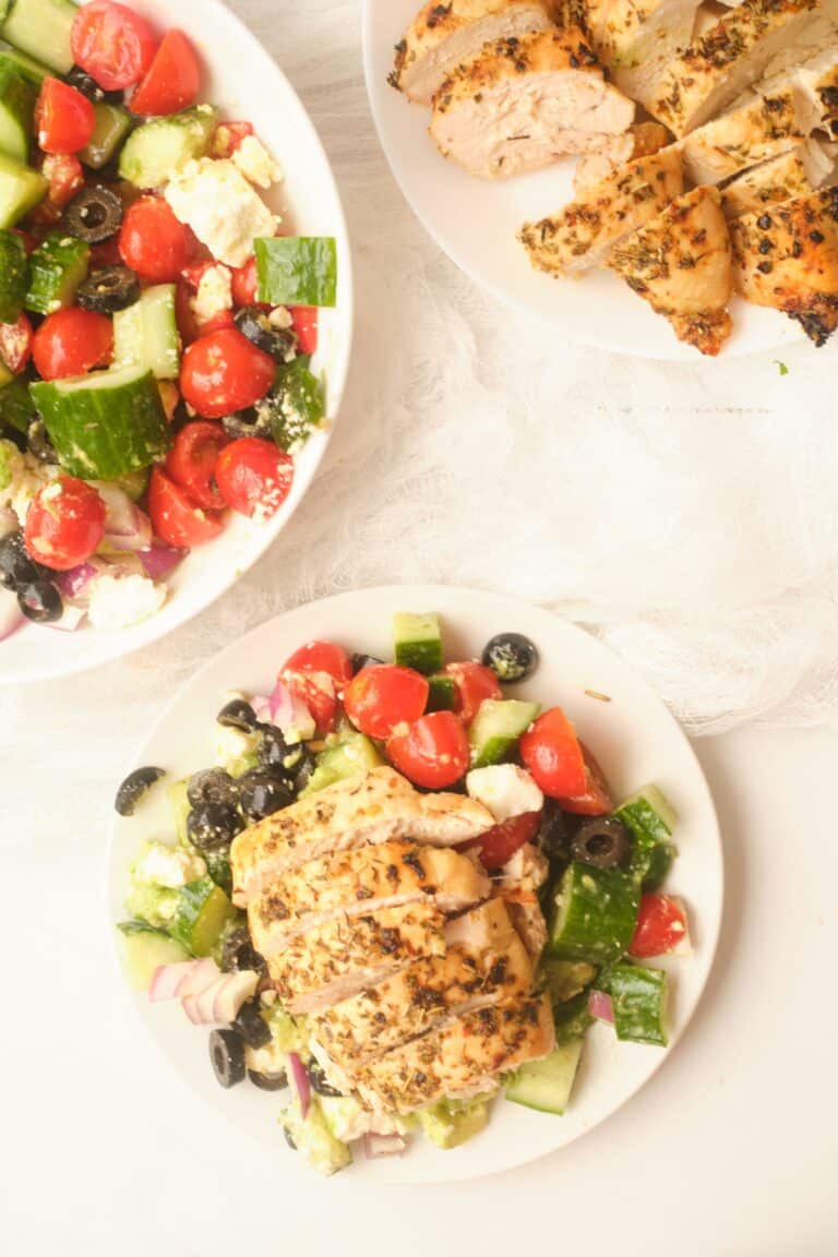 Grilled chicken on a plate with Greek salad mixed with dressing.