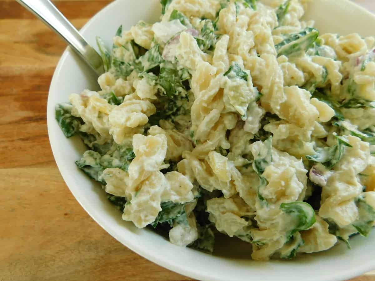 Spinach and artichoke pasta salad in white bowl