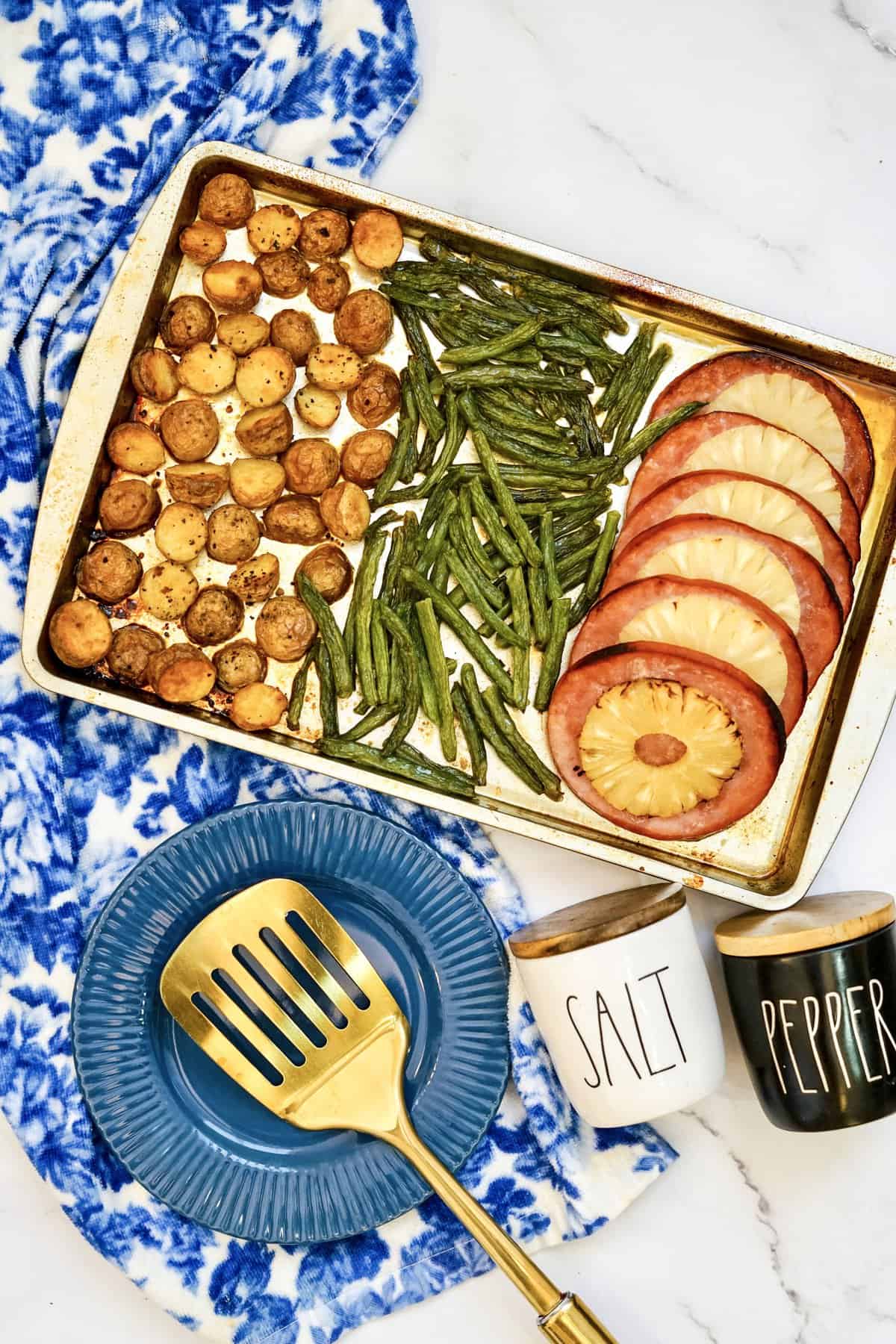 Ham and pineapple sheet pan dinner with roasted mini potatoes and green beans, a spatula lifting a portion