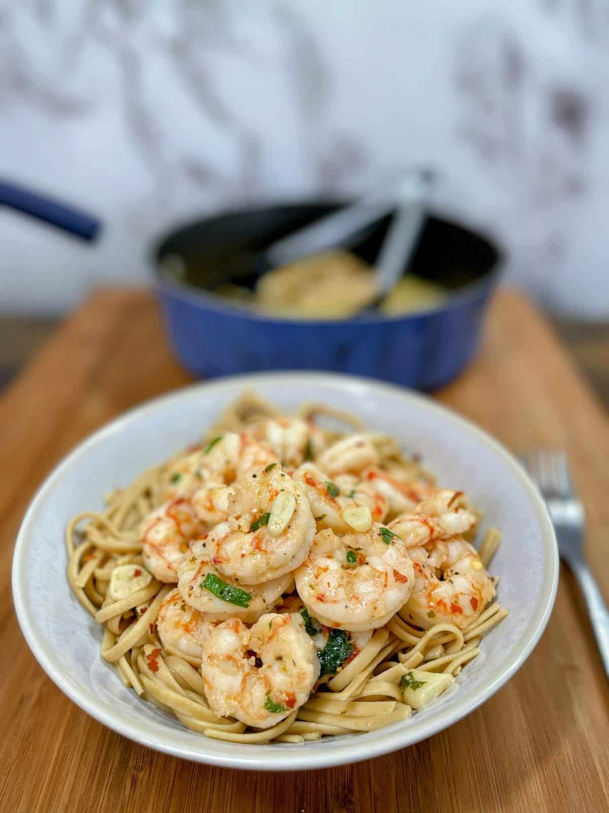 shrimp scampi with noodles in pasta bowl cooking pot in background