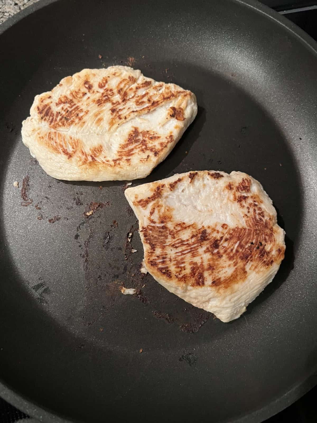 chicken breast cooking in non-stick pan