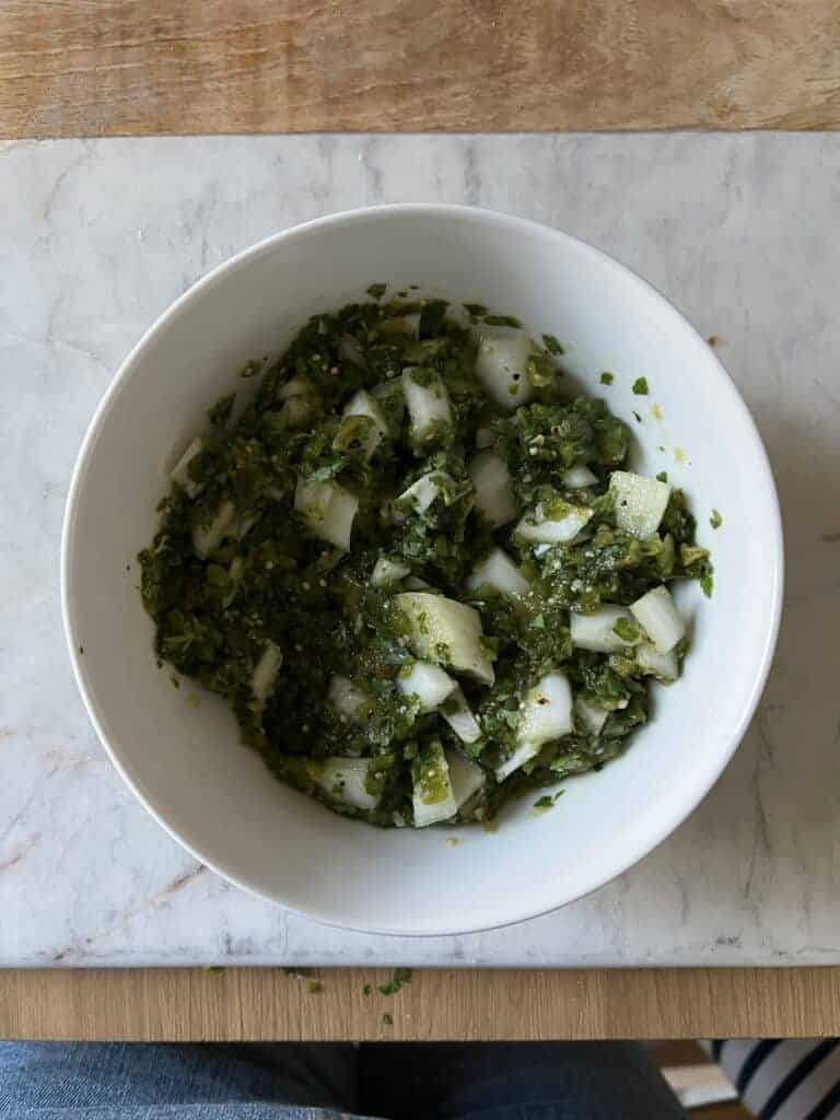 Roasted poblano salsa made with tomatillos, a chunky green salsa with diced white onion, in a white bowl.