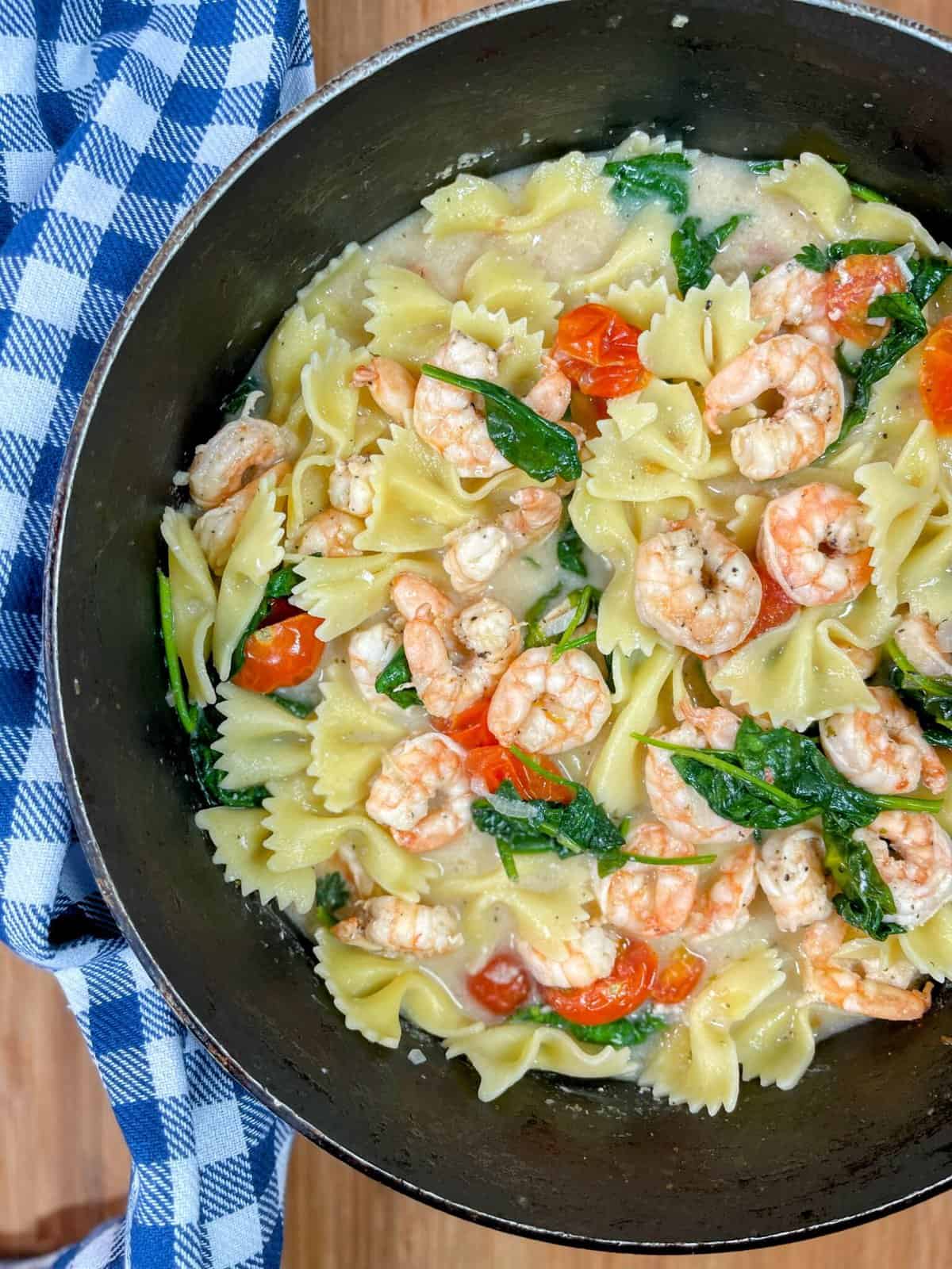 Cooked shrimp simmering with pasta, spinach and cherry tomatoes in a pot