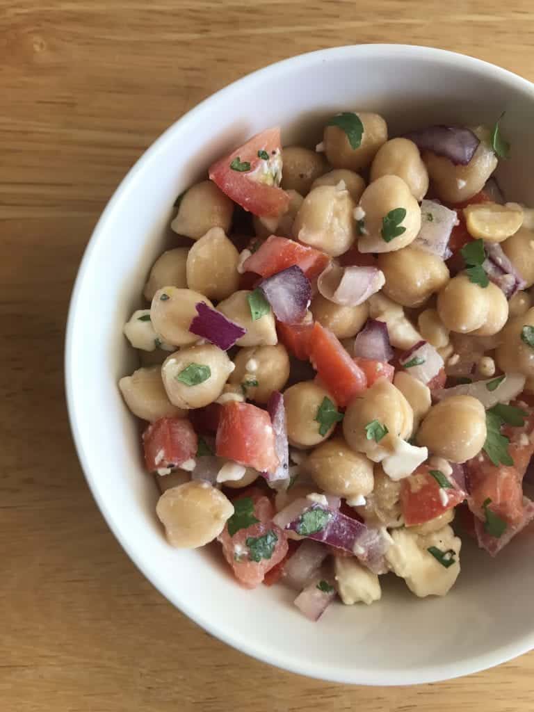 Bowl of chickpea salad mixed with herbs, tomatoes, red onions and feta cheese. 