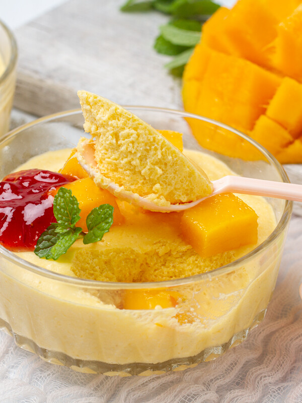 Yellow mango mousse sitting in a clear bowl with a spoon.