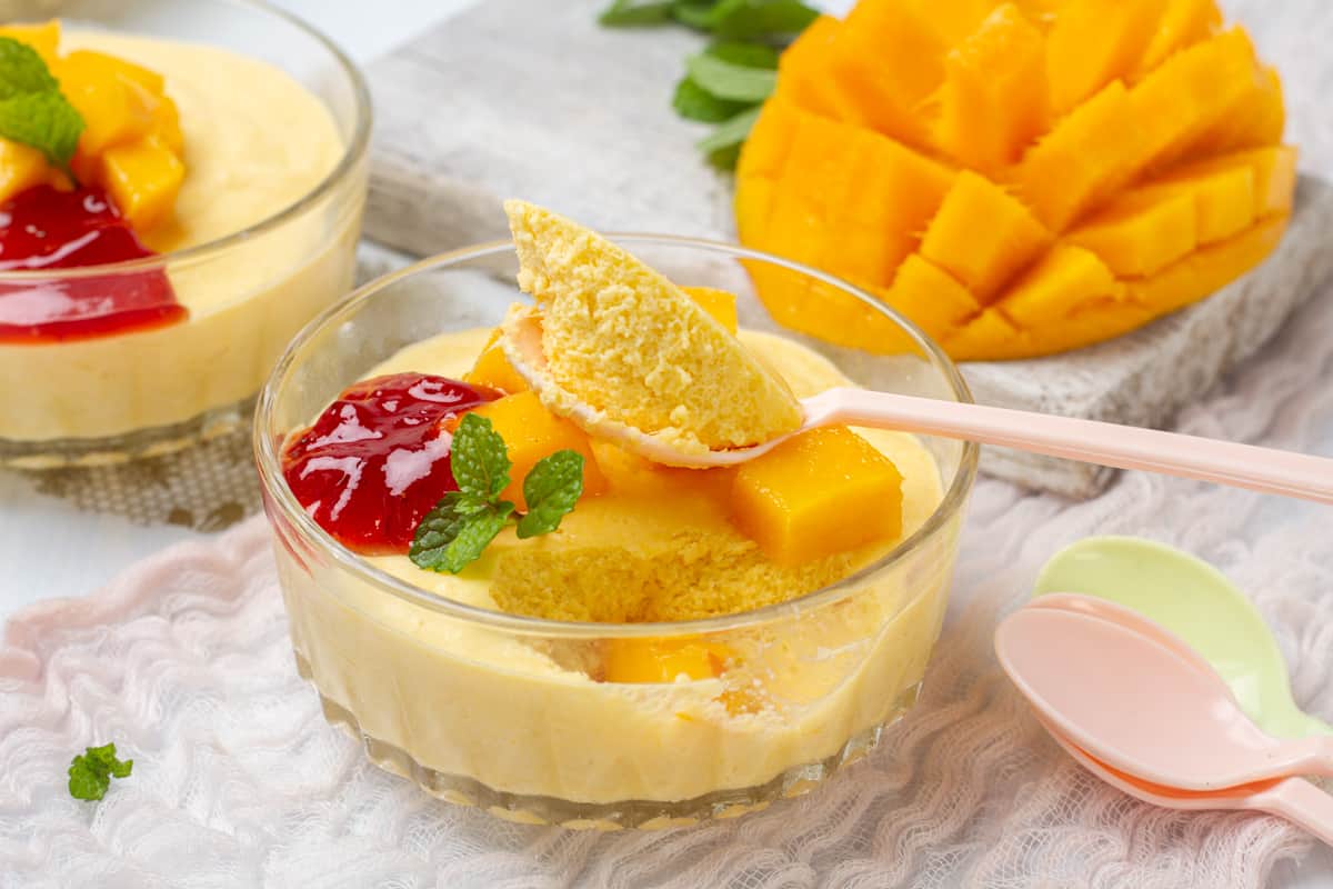 Yellow mango mousse sitting in a clear bowl with a spoon.