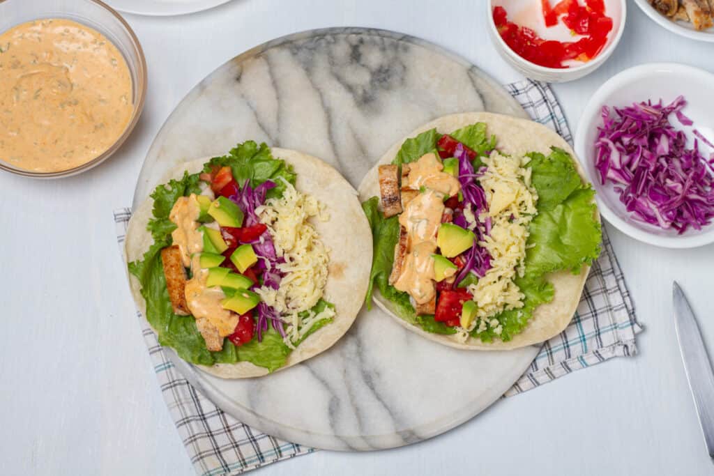 Tortillas filled with lettuce, cabbage, tomatoes, avocado, and chicken in chipotle sauce drizzle.
