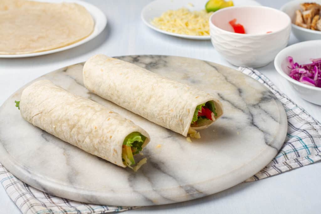 Two rolled chipotle ranch grilled chicken burritos on a cutting board.