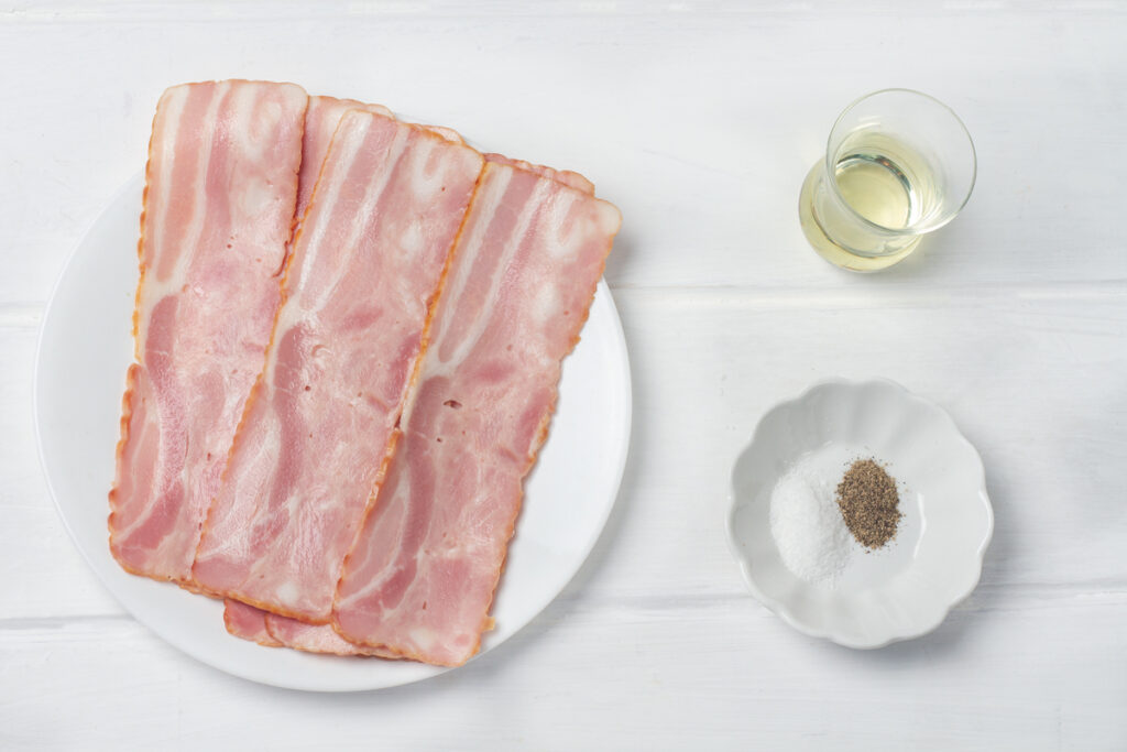 Turkey bacon on a plate, olive oil in a cup, salt and black pepper in a dish. 
