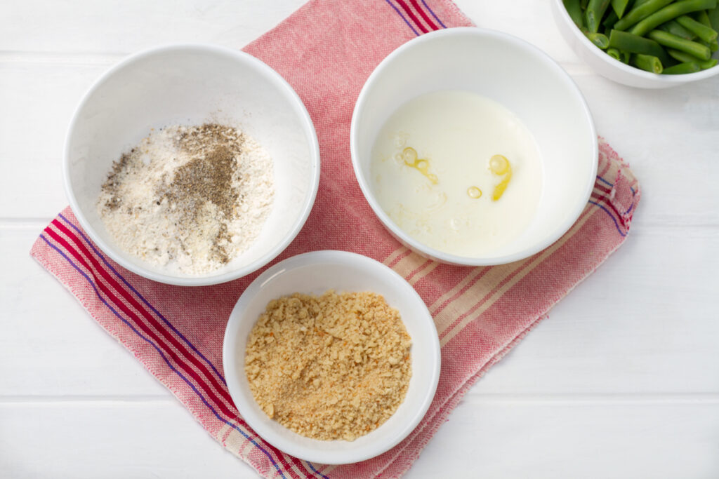 A dish of spices mixed in flour, a dish of milk and egg whites mixed, and a dish of Panko bread crumbs. 