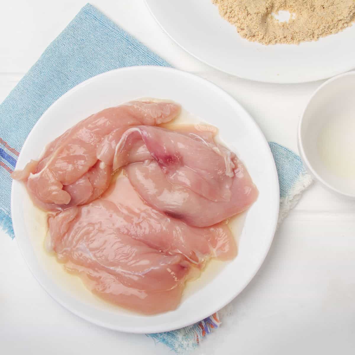 Raw chicken breasts coated in egg whites.