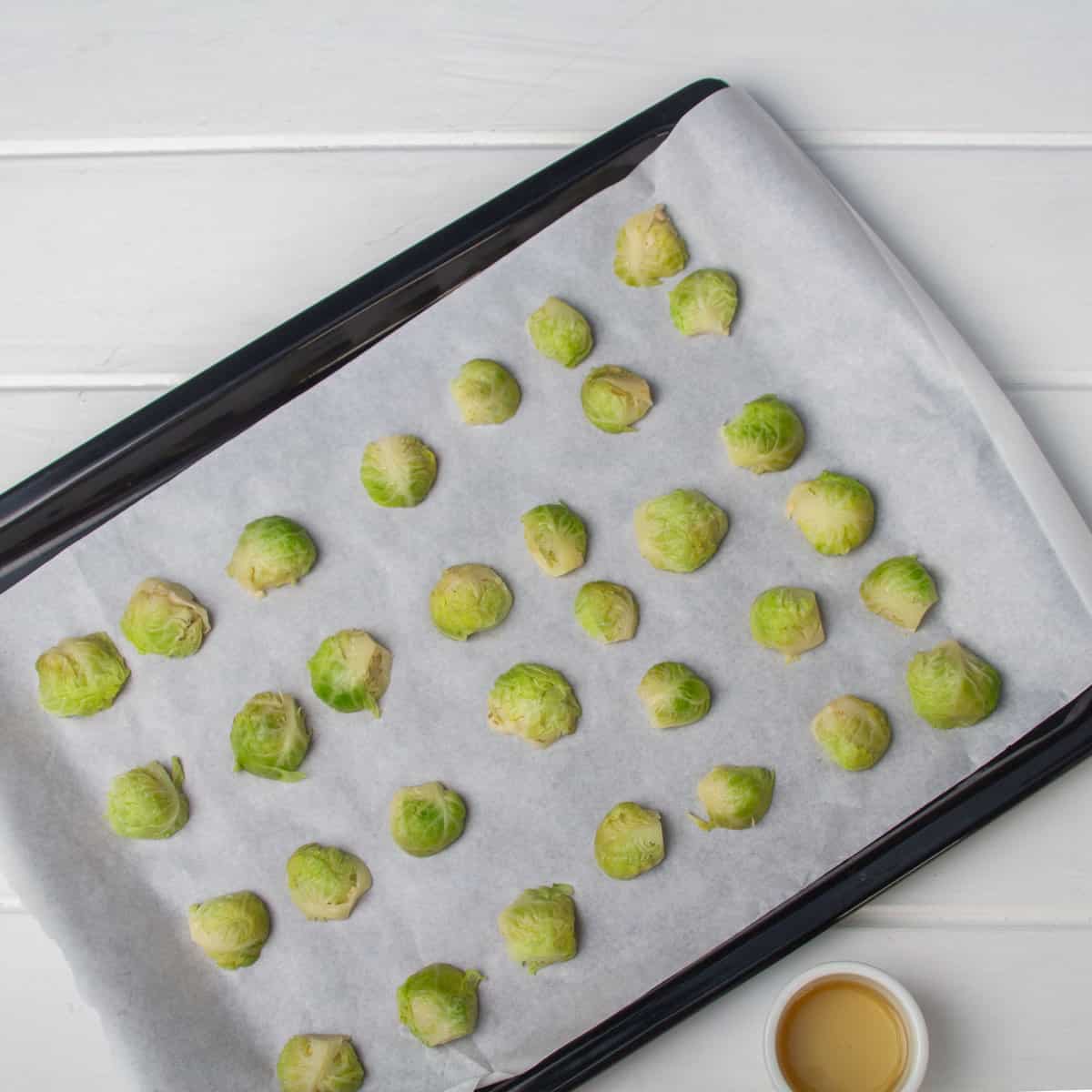 Halved brussel sprouts spread evenly on a parchment-lined baking sheet. 