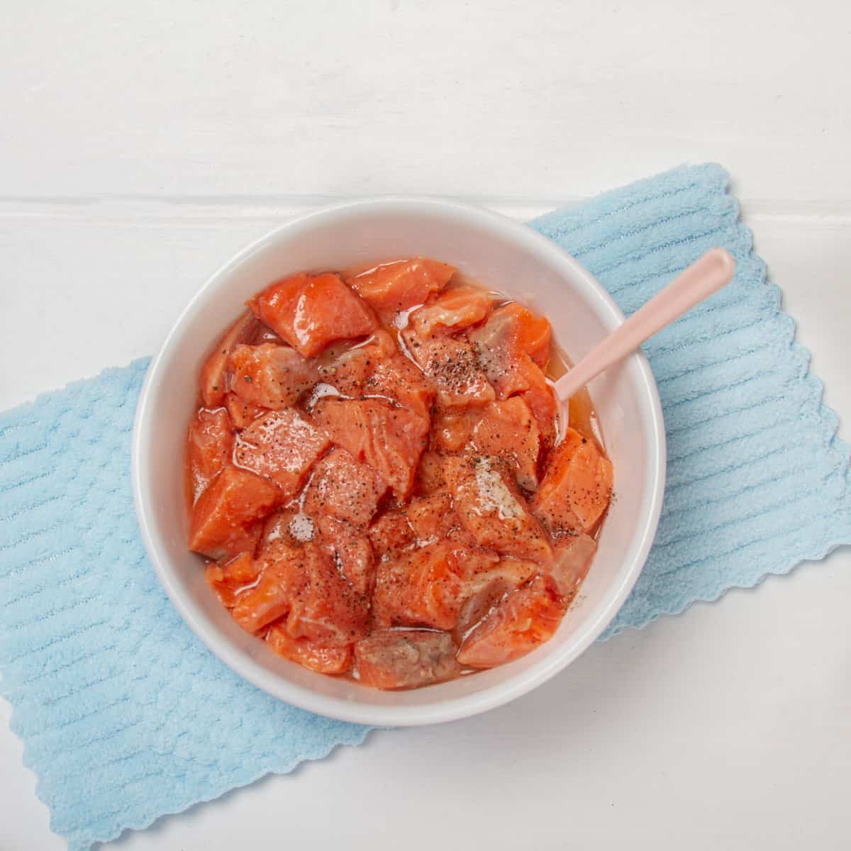 Chunks of fresh salmon coated with lime juice, salt and pepper in a bowl.