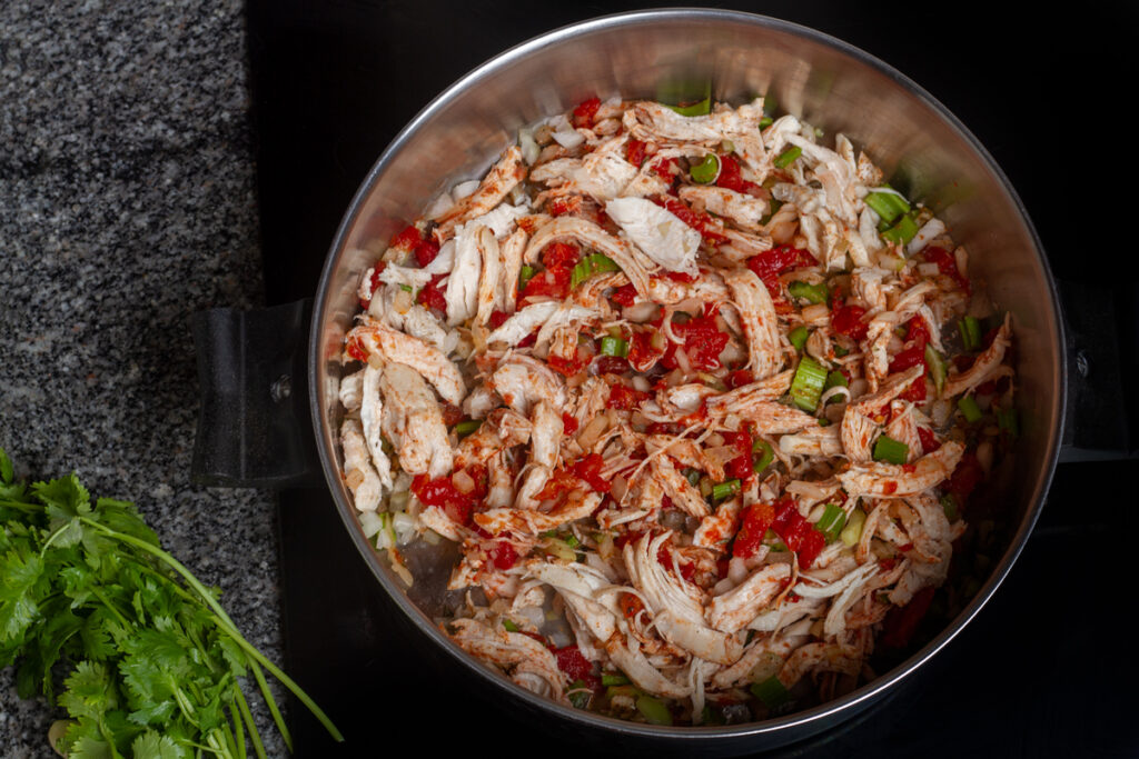 Shredded chicken, spices, tomatoes, and celery cooking in a pot. 