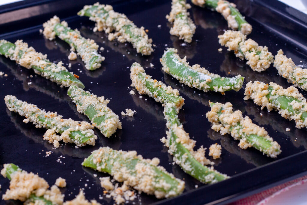Breaded green beans cooking on an baking tray. 