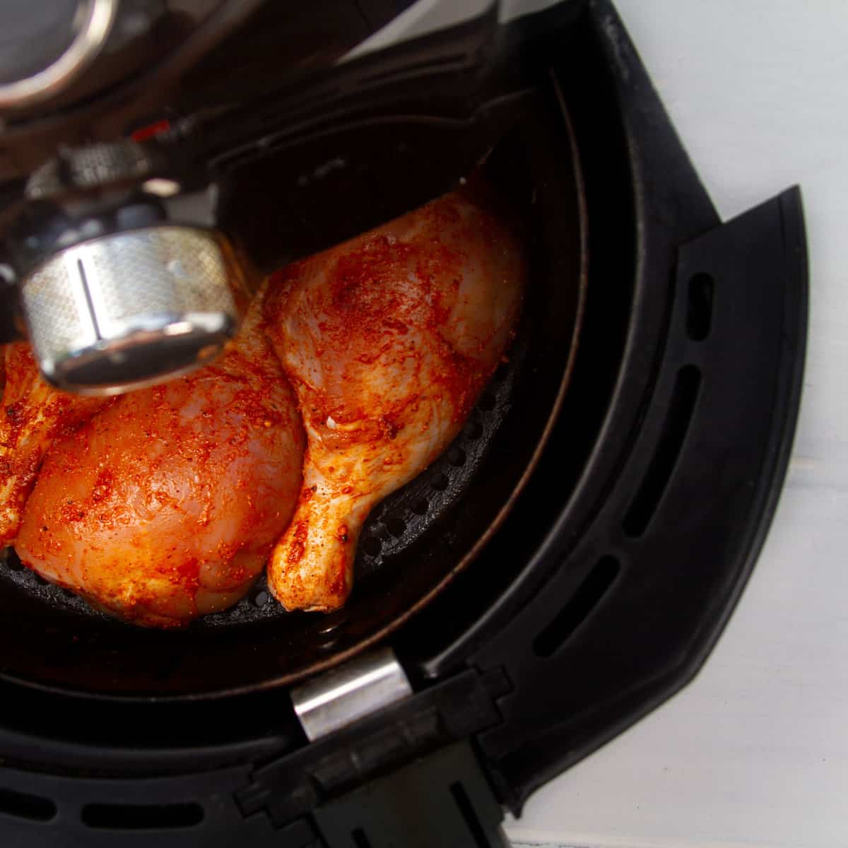 Seasoned chicken thighs in an air fryer basket.