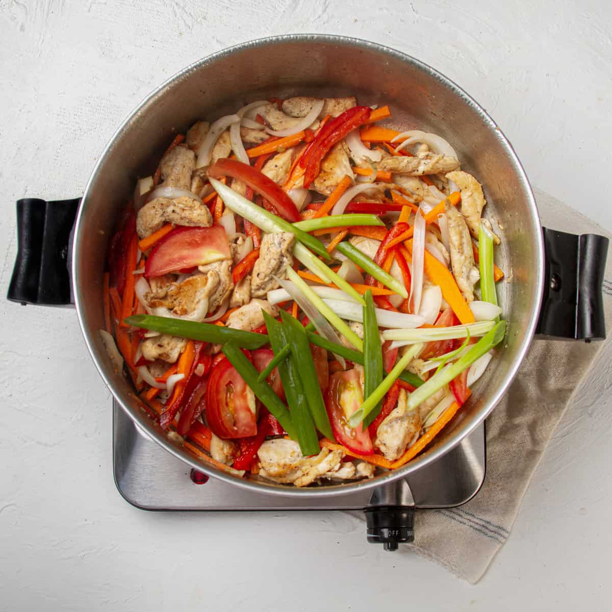Chicken and matchstick veggies, including carrot, bell pepper, white onion, and green onion, stir-frying in a pan. 