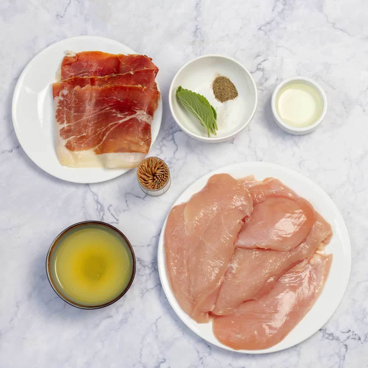 Ingredients of raw chicken cutlets, prosciutto, sage leaves, olive oil and lemon juice, and spices in separate dishes. 
