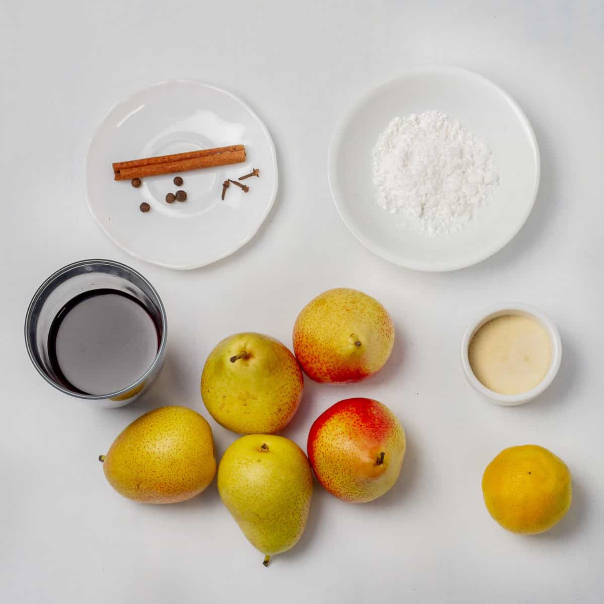 Whole pears, stevia, cinnamon sticks, spices, and red wine ingredients in separate dishes.