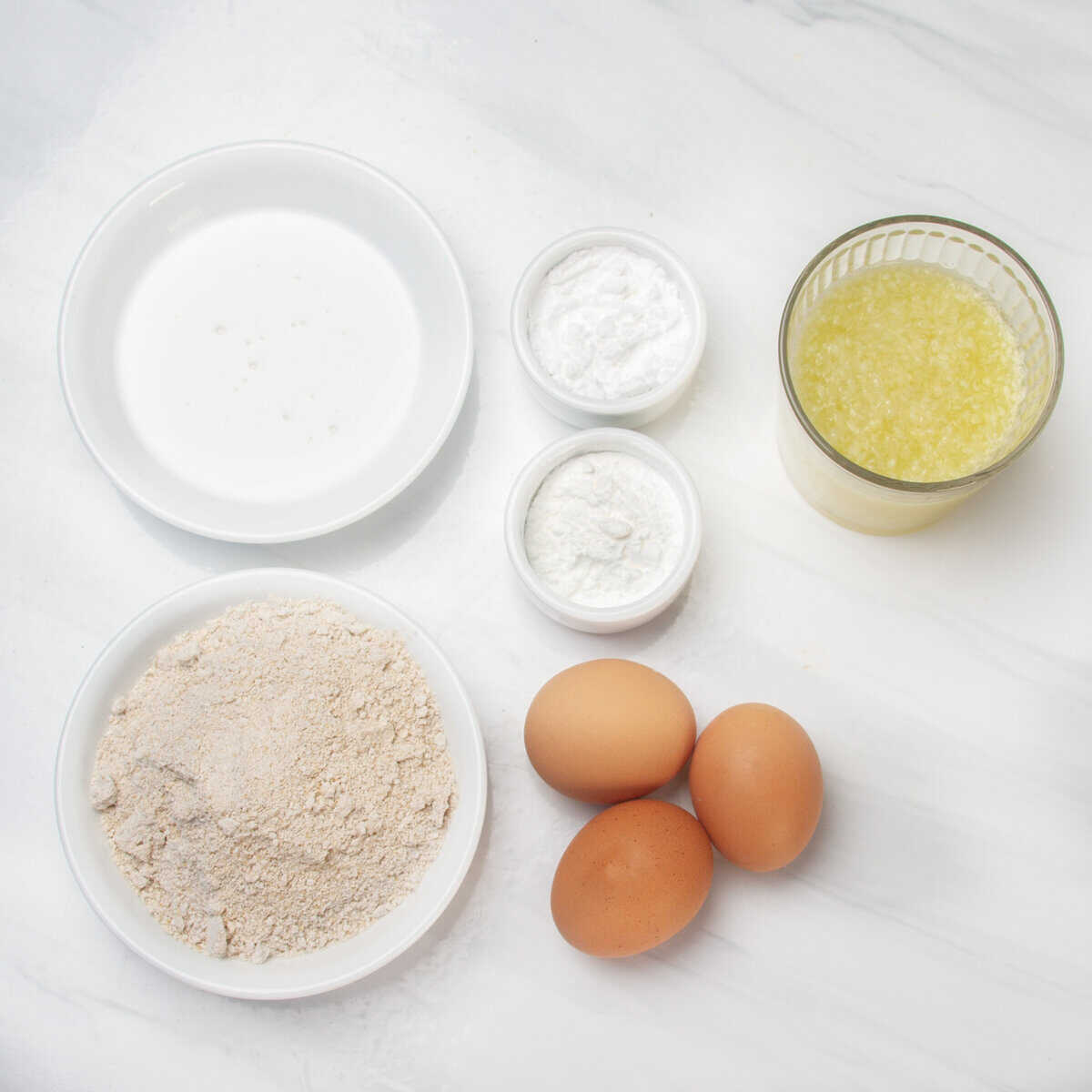 Oat flour, stevia, coconut cream, eggs, lemons, lemon juice, and tapioca starch in separate dishes.