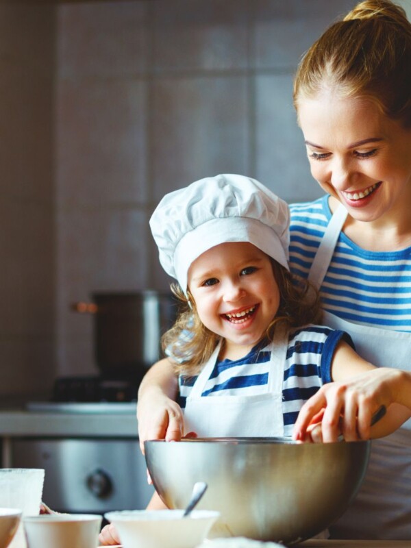 Mother and daughter stirring spoon in metal mixing bowl