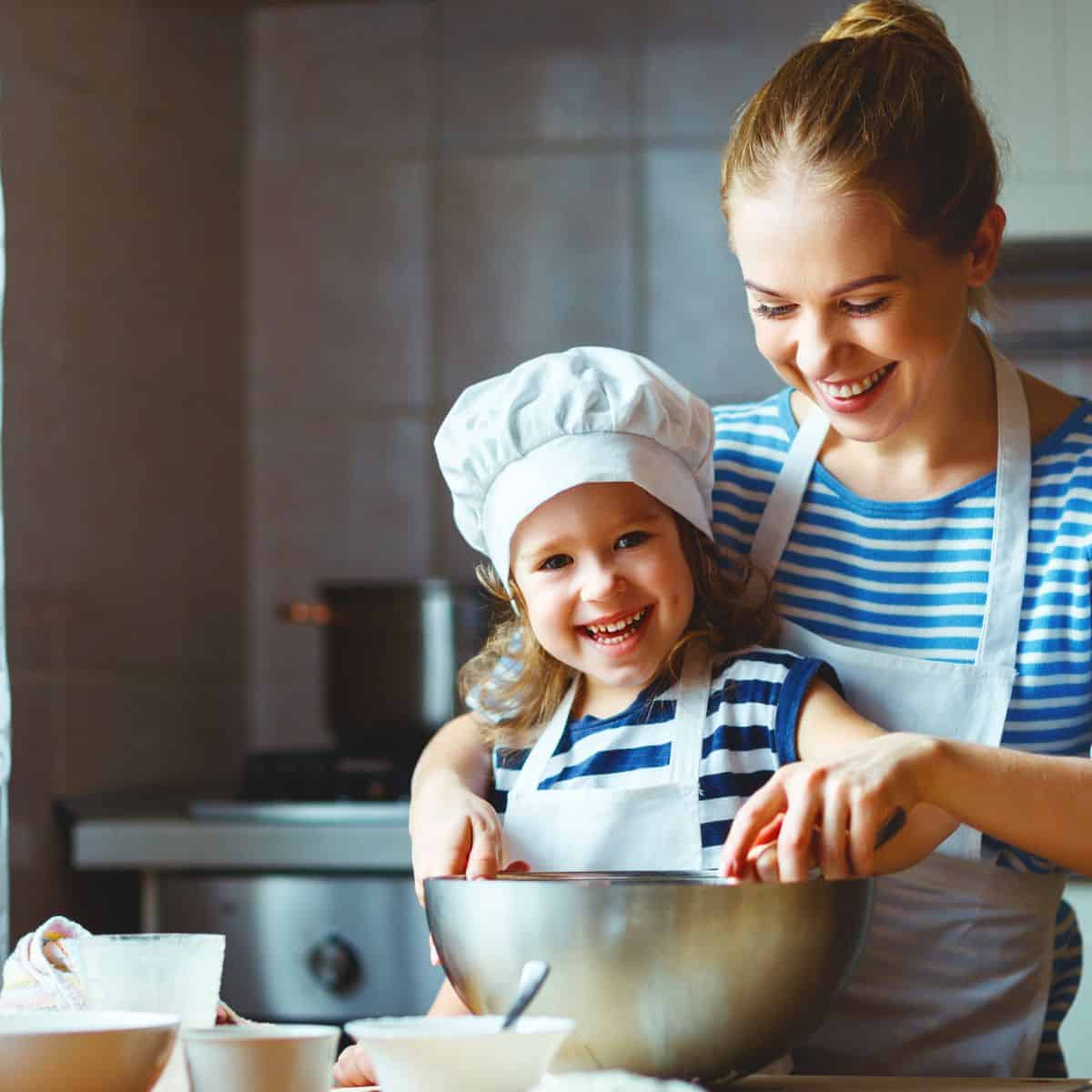 Mother and daughter stirring spoon in metal mixing bowl