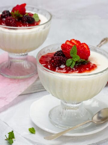 Rich and creamy panna cotta in two dishes, topped with fresh berries and mint.