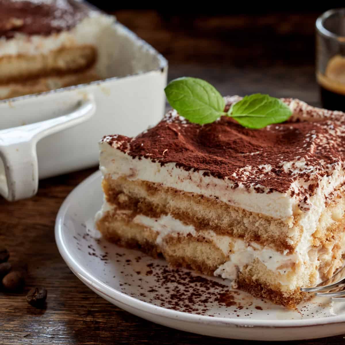 Gourmet tiramisu Italian dessert topped with a sprig of mint served on a plate at table in a side view
