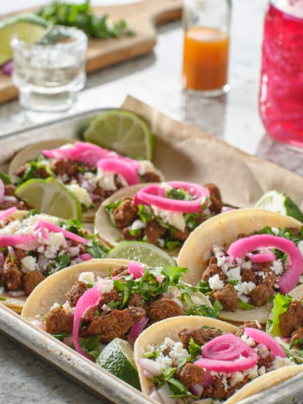 tray of carne asada tacos topped with pickled onions and cojita cheese