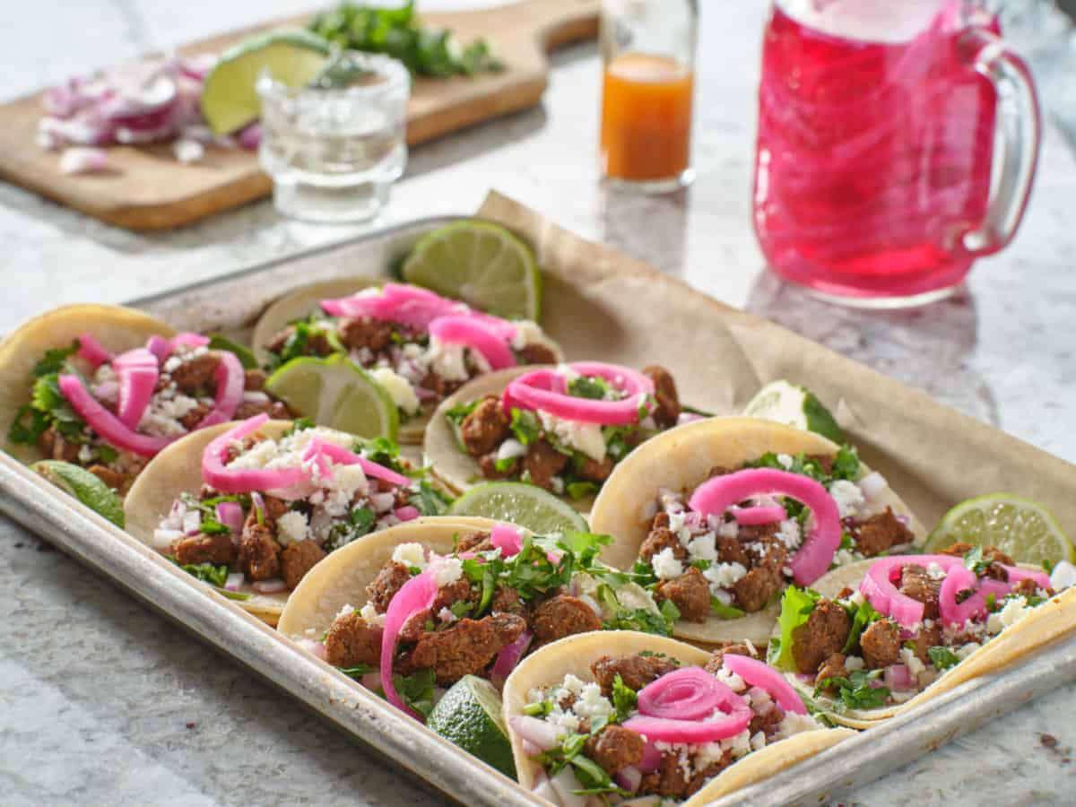 tray of carne asada tacos topped with pickled onions and cojita cheese