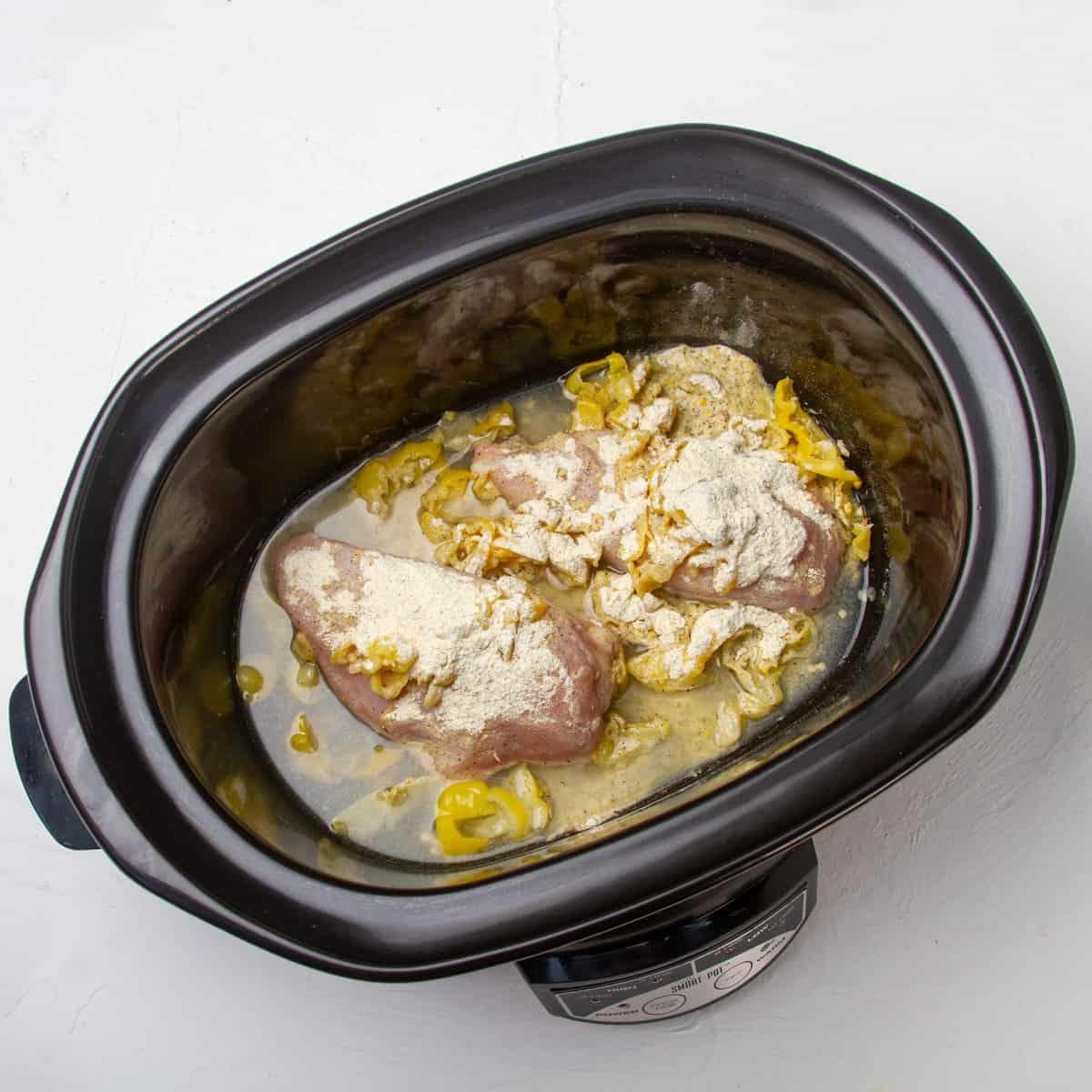 Raw chicken, spices, pickled peppers, and gravy mix in a slow cooker.