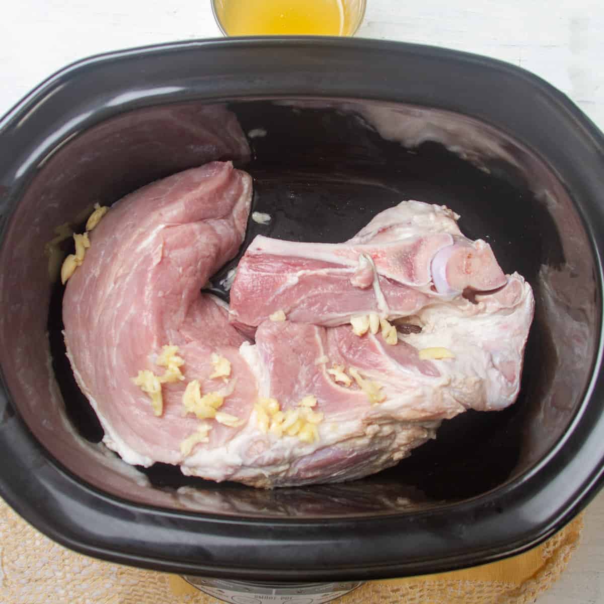 Add prepped pork shoulder and garlic to the slow cooker.
