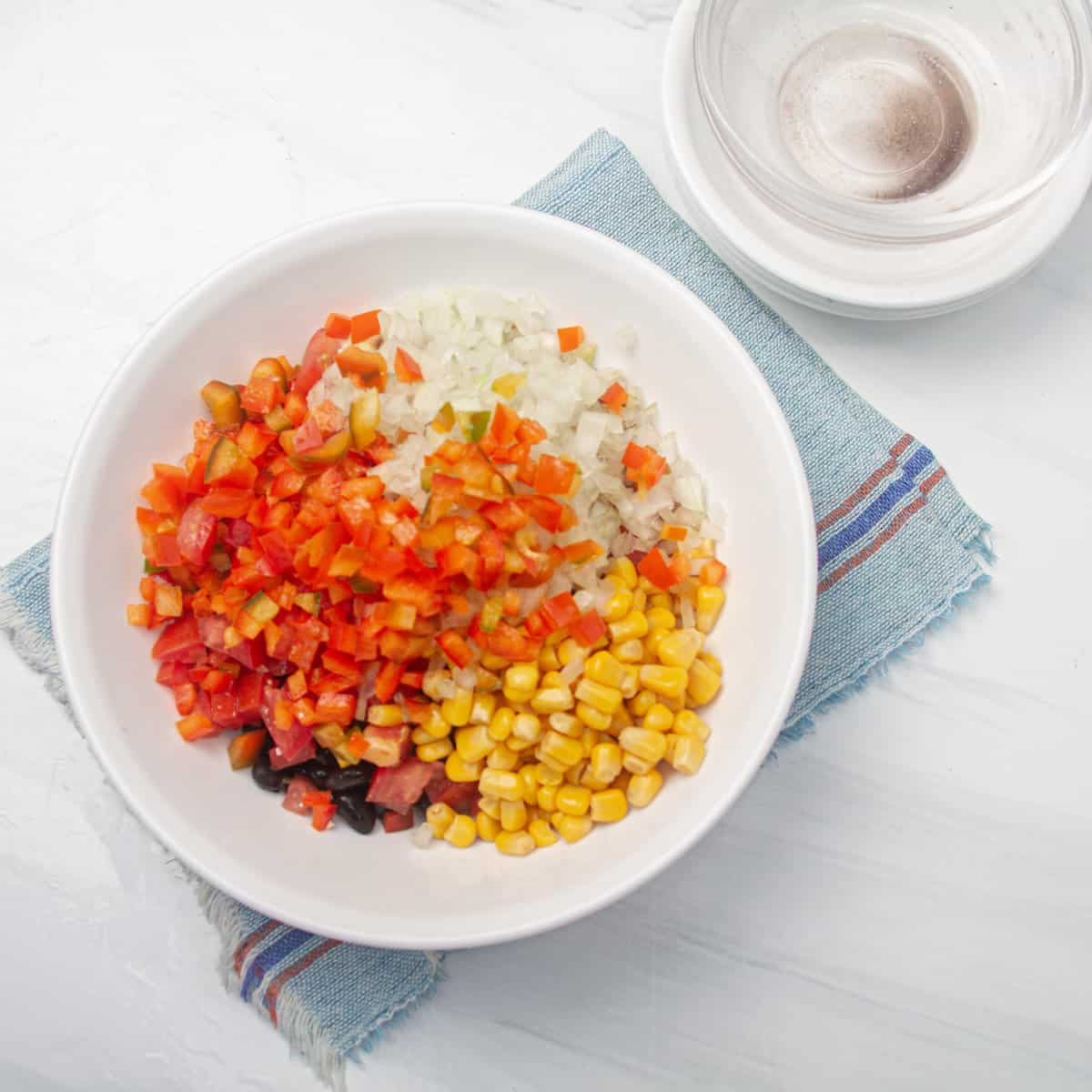 Drained beans, corn, diced tomatoes, chopped onions, and bell peppers combined in a bowl.