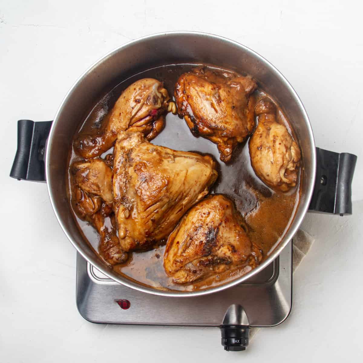 Chicken simmering in shoyu sauce in a hot pan.