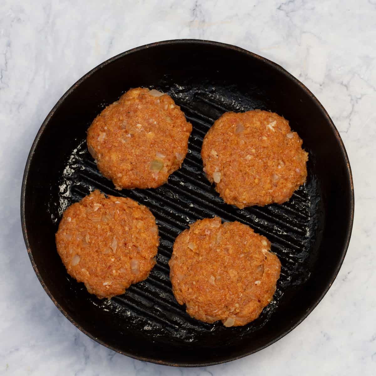 Raw chicken burger patties cooking in a hot skillet.