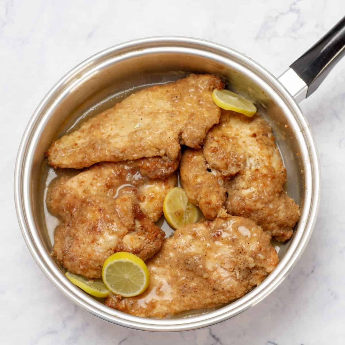 Chicken Francese cooking in a hot pan with lemon slices.