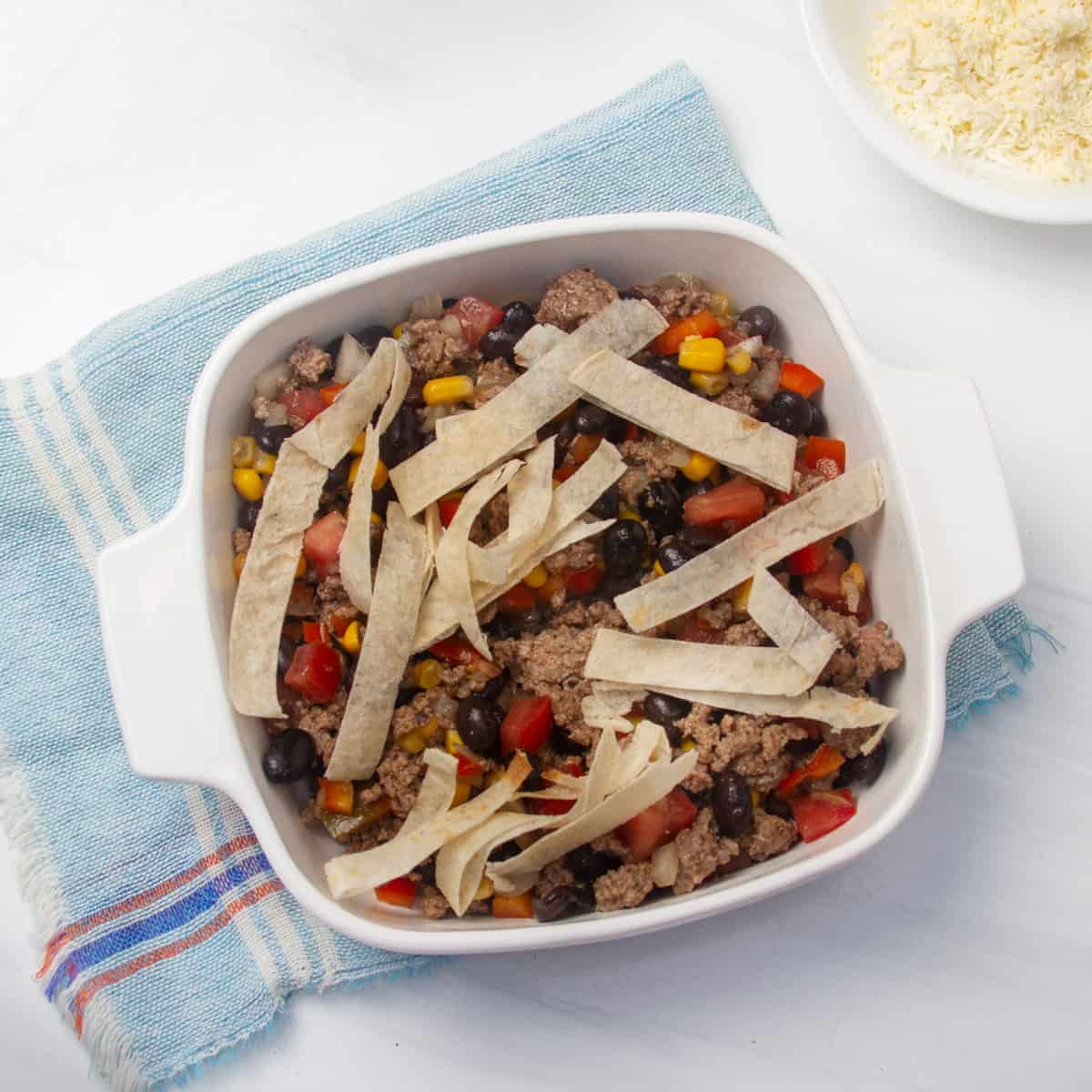 Ground beef and veggie mixture topped with tortilla strips in a baking dish.