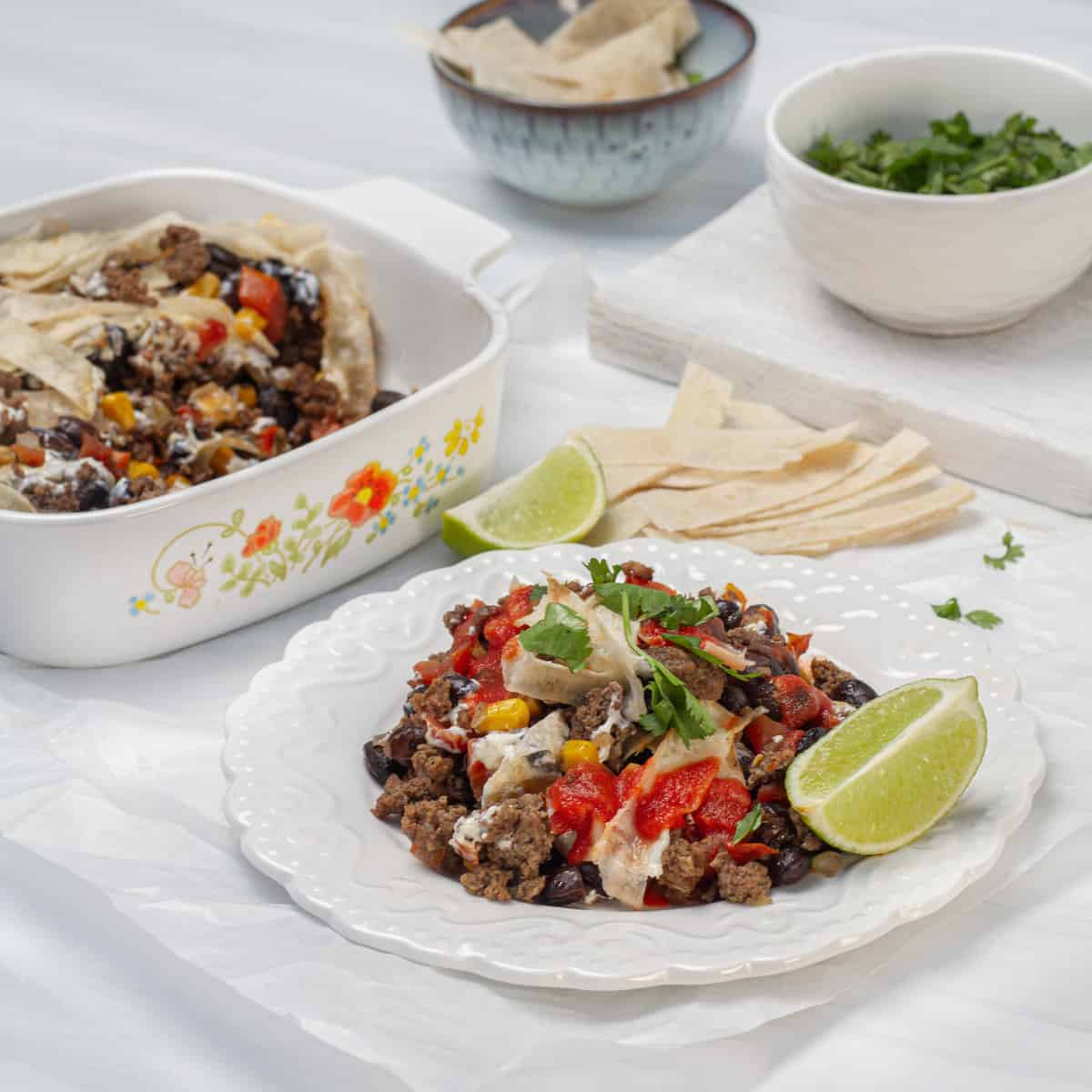 Cheesy ground beef taco casserole on a plate, garnished with a lemon wedge and fresh herbs.