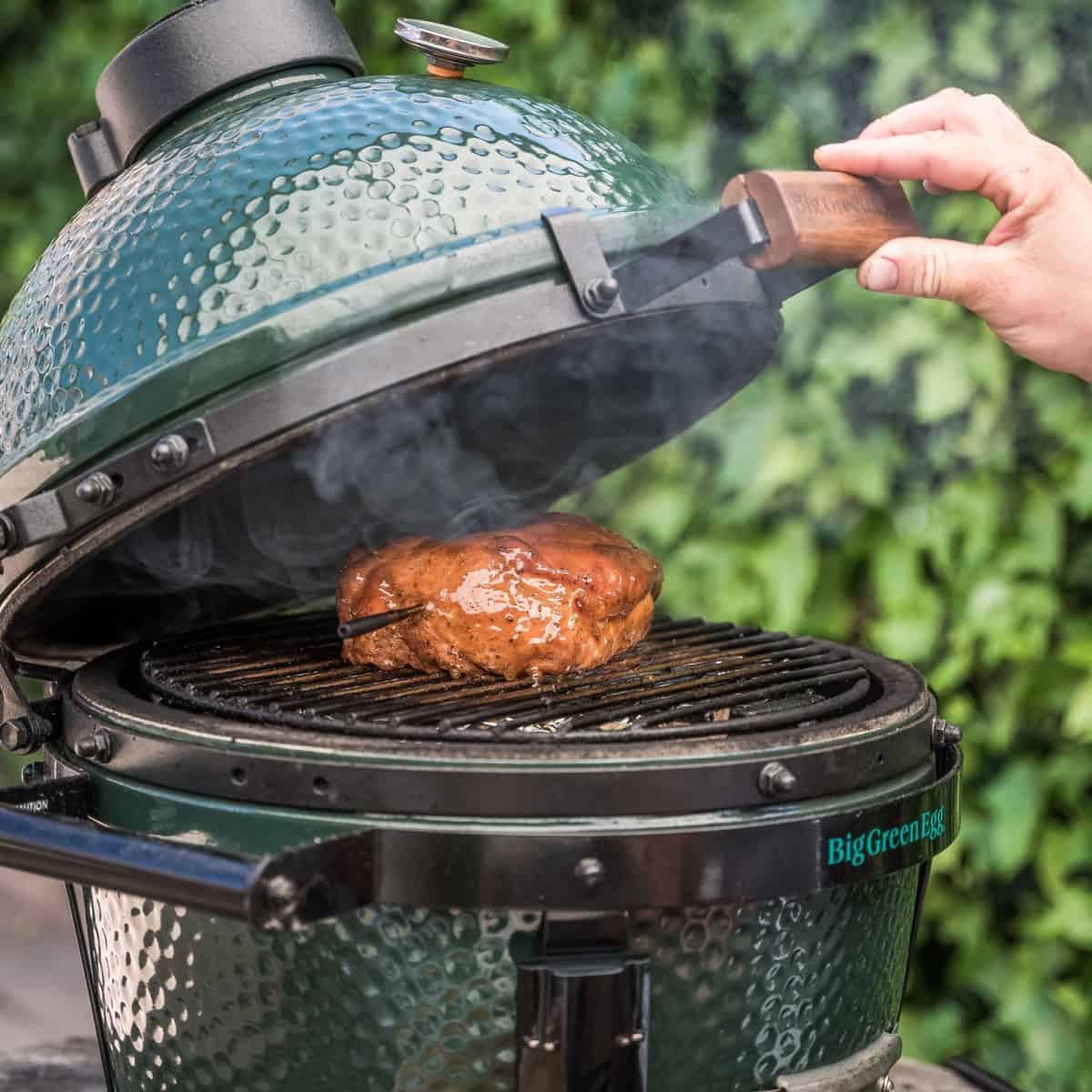 hand opening big green egg with meat smoking