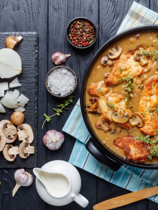 Chicken Marsala cooked in cast iron with fresh ingredients on chopping board next to cooking dish