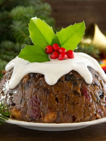 Christmas pudding on white plate topped with leaves