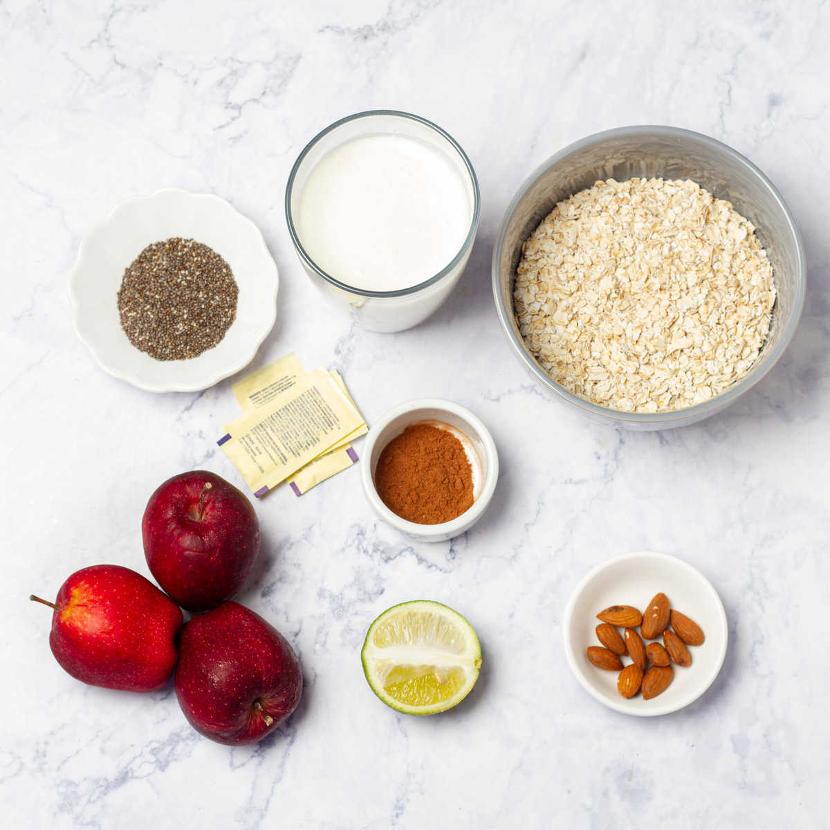 Apples, oats, chia seeds, milk, spices, and sweetener in separate dishes.