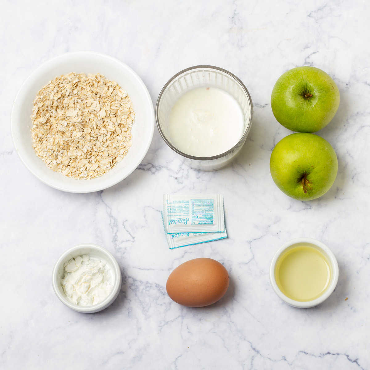 Oats, milk, apples, egg, baking powder and spices in separate dishes. 