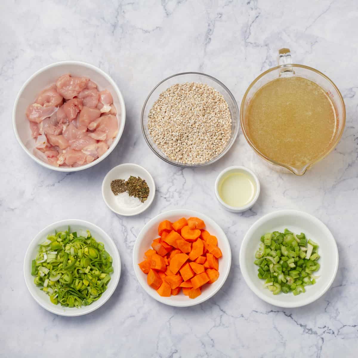 Ingredients of chicken breast and broth, chopped onion, carrots, and celery, and spices in separate dishes. 