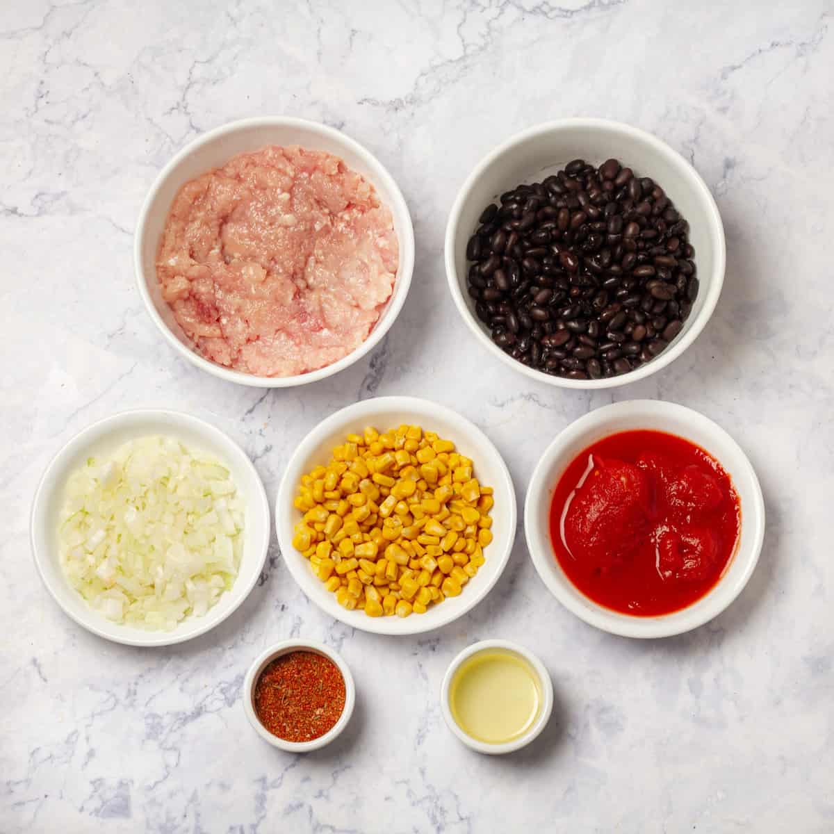 Ingredients of ground turkey, canned black beans, diced tomatoes, corn, onion, and spices in separate dishes. 