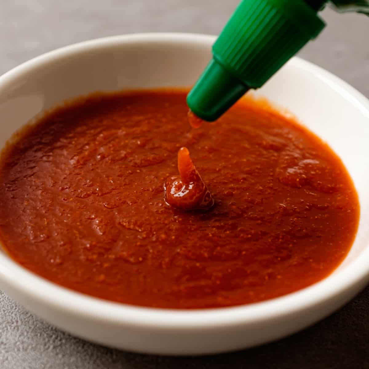 sriracha pouring from bottle into white dish