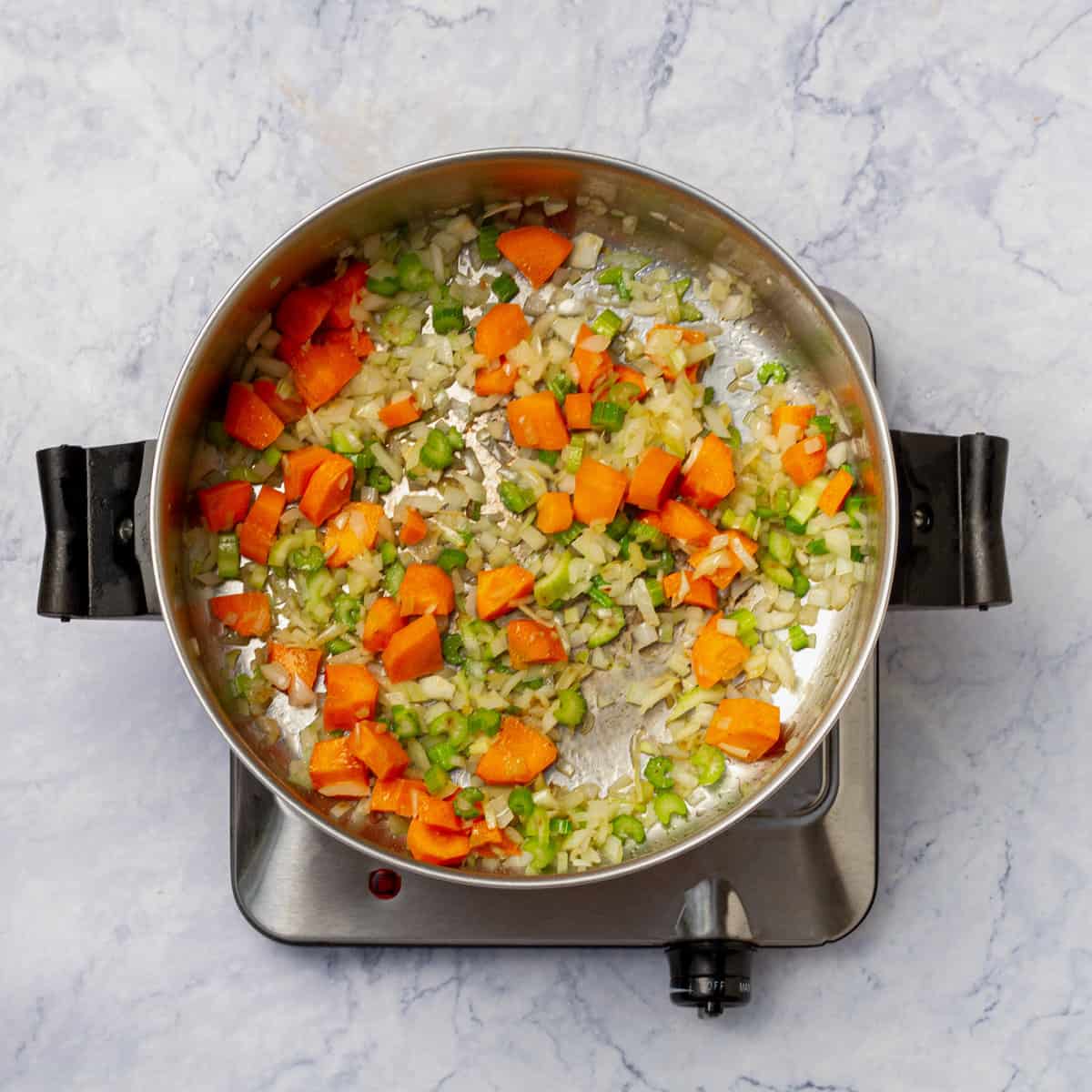 Carrots, celery, and onion sautéeing in a pan.